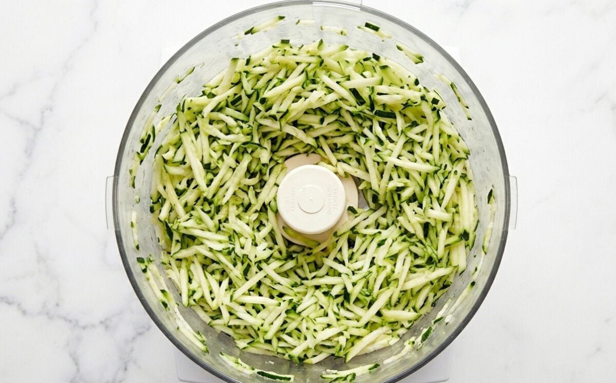 Shredded zucchini in bowl of food processor. 