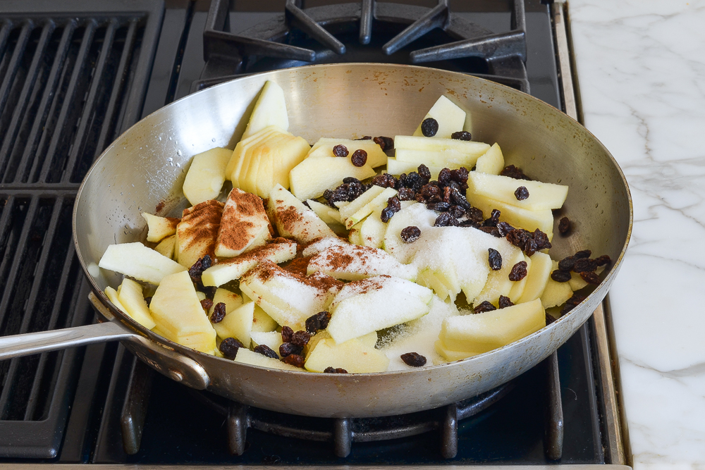 combining apples, raisins, sugar, brandy and cinnamon in pan