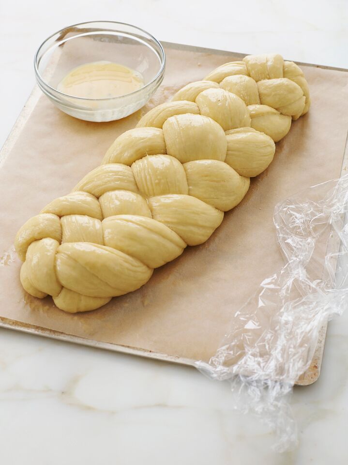 Braided challah dough on a lined baking sheet.