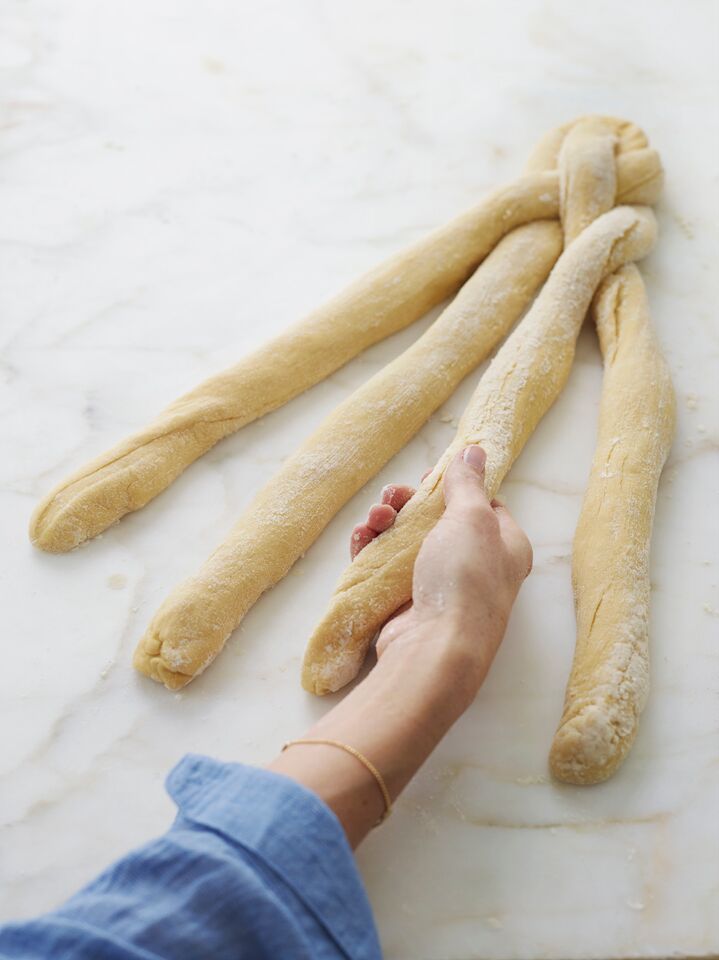 Person grabbing the third of four strands of challah dough.