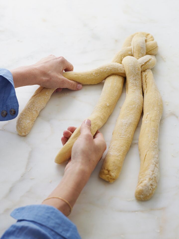 Person grabbing the first and second strands of challah dough out of four.