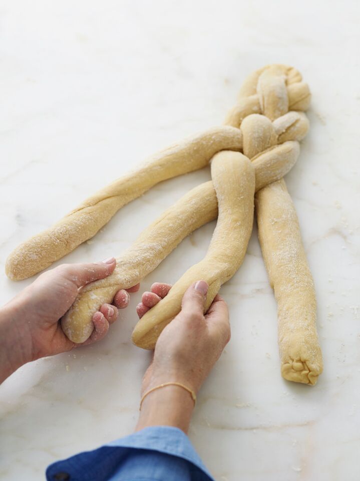 Person grabbing the two middle strands of challah dough out of four.