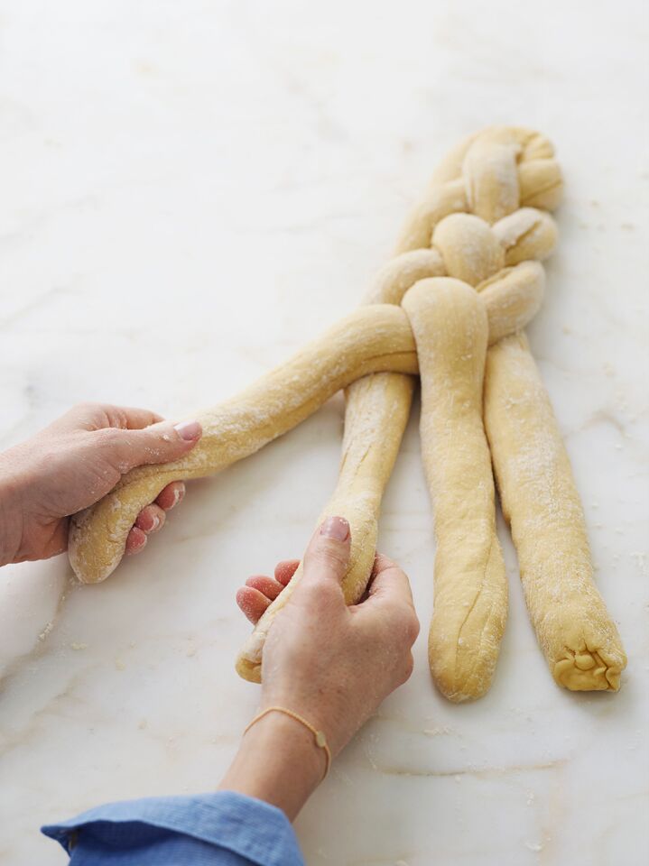Person grabbing the first two strands of challah dough out of four.