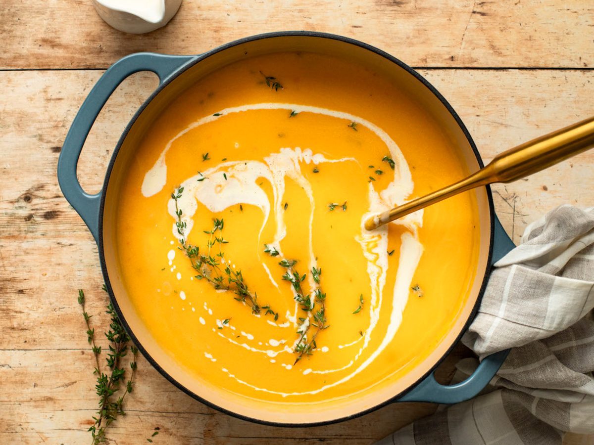 Ladle in a pot of butternut squash soup drizzled with cream.