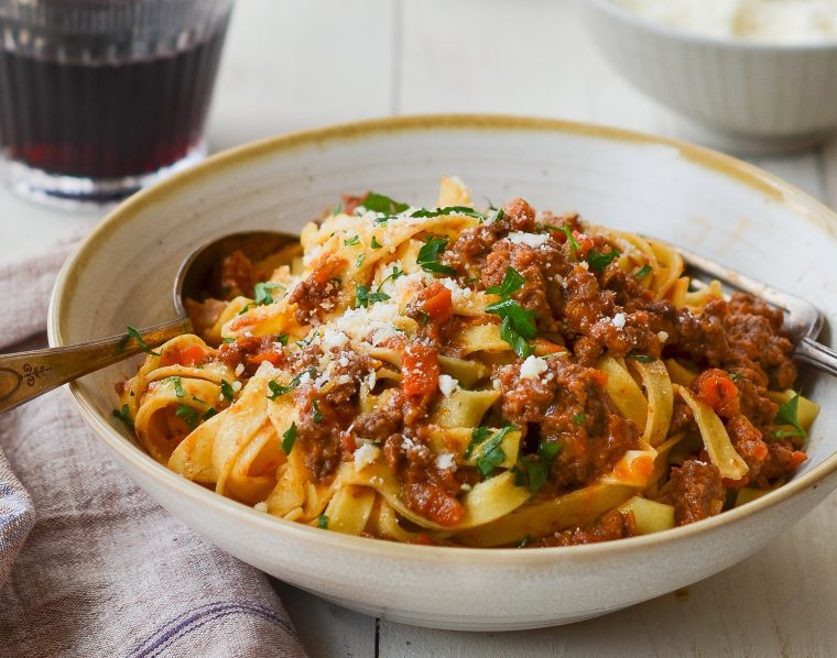 Bolognese with pasta in bowl with glass of wine