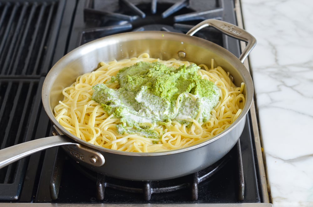 adding pesto and cream to linguine