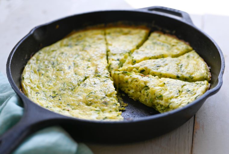 Partially sliced and served zucchini frittata in a skillet.