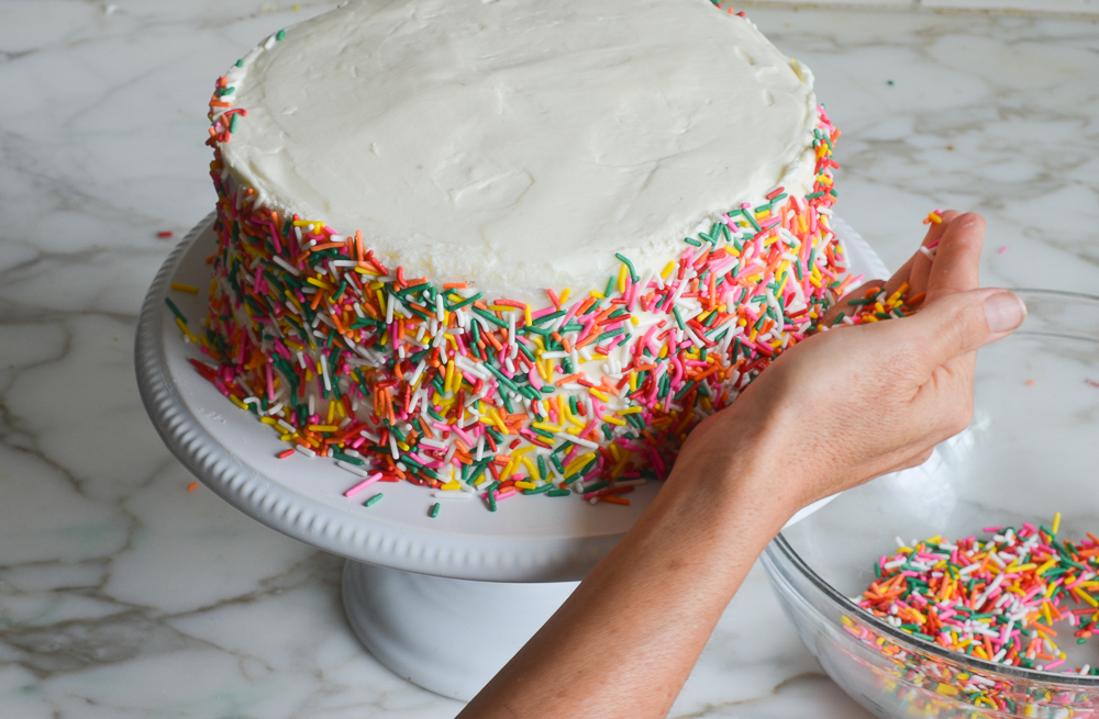 pressing the sprinkles onto the sides of the cake