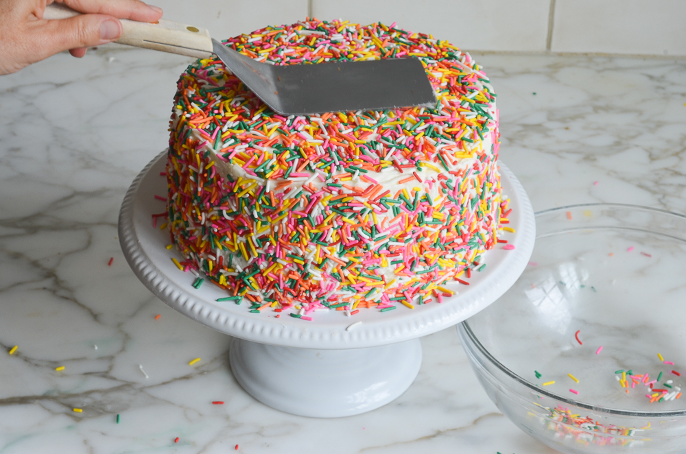 pressing sprinkles onto the top of the cake