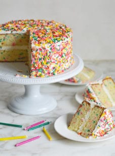 Slices of rainbow sprinkle Funfetti cake on plates next to the rest of the cake.