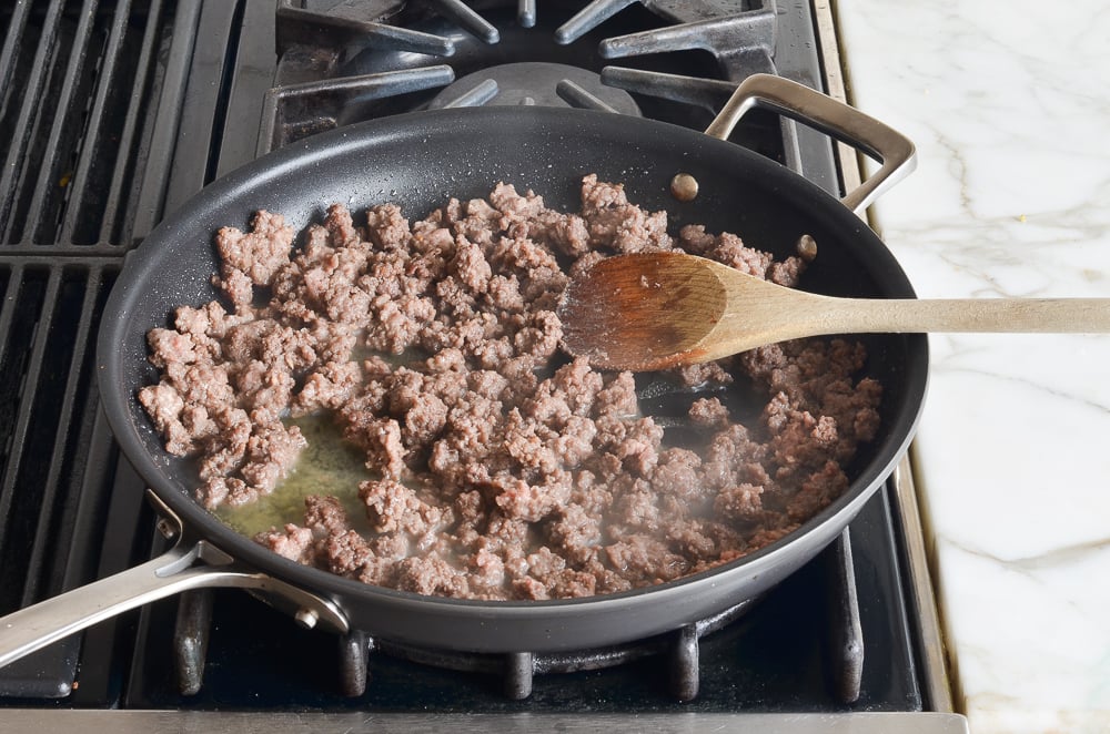 Wooden spoon in a skillet of browned beef.