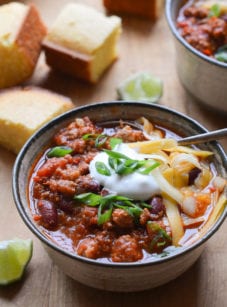 Spoon in a bowl of turkey chili topped with cheese and sour cream.