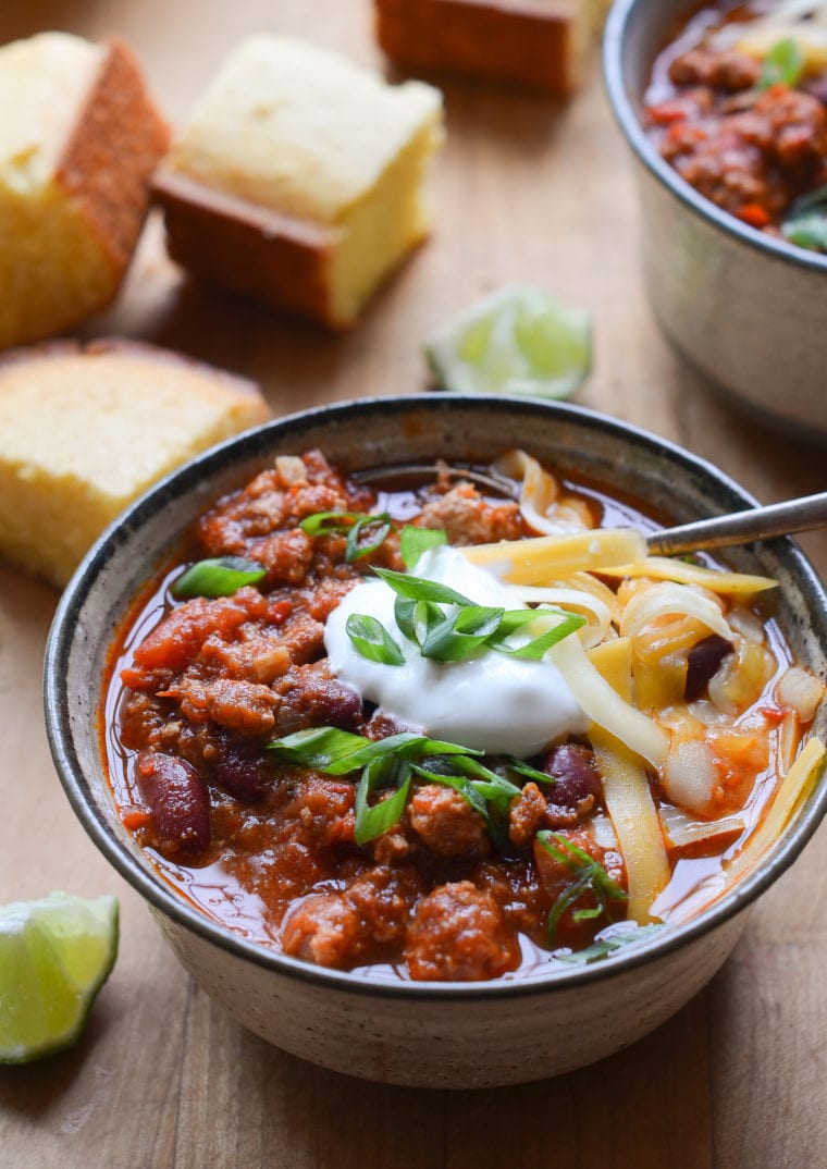 Spoon in a bowl of turkey chili topped with cheese and sour cream.