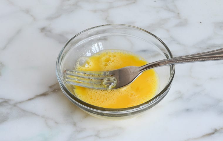 Egg wash in a bowl with a fork.