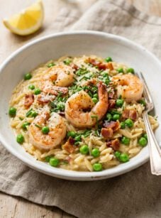 Orzo risotto with shrimp, bacon, and peas in white ceramic bowl.
