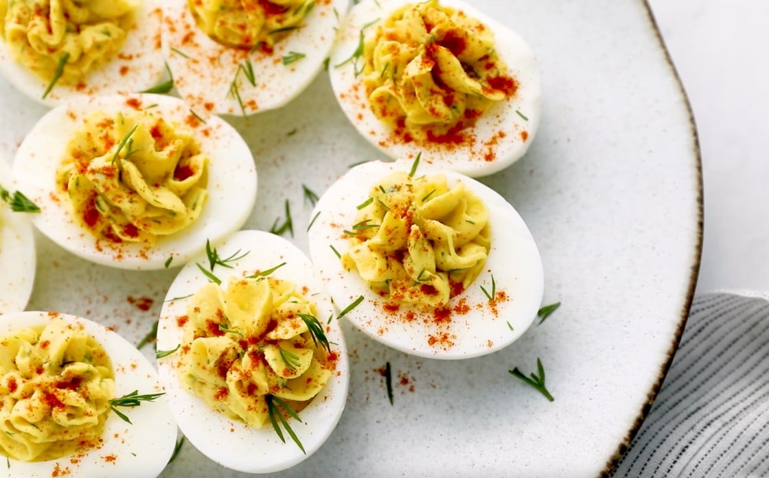 A plate of deviled eggs topped with paprika and herbs.
