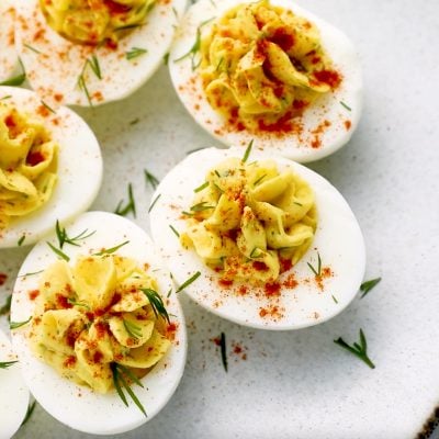 A plate of deviled eggs topped with paprika and herbs.