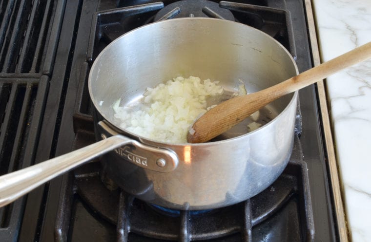 Wooden spoon stirring onions in a pan.