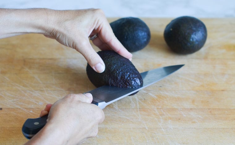 Person cutting an avocado from the thinner side.