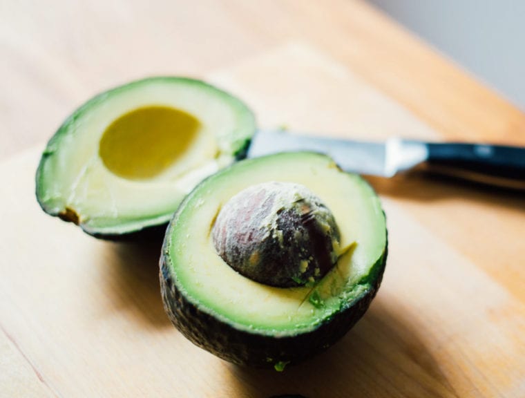 Halved avocado on a cutting board with a knife.