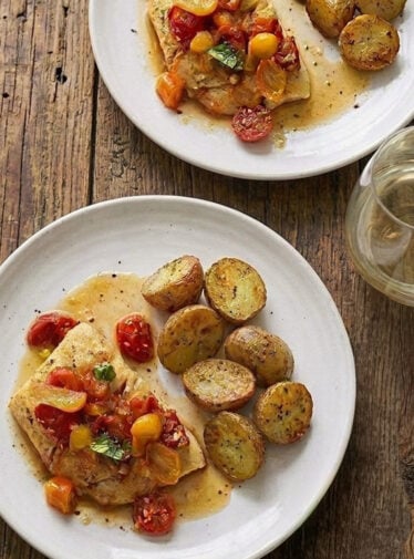 Pan seared halibut with cherry tomatoes and basil on ceramic white plates.