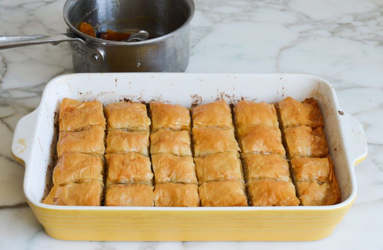 drizzling honey syrup over baked baklava