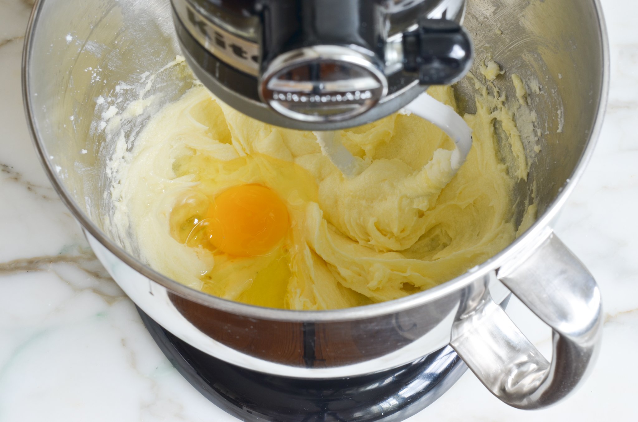 Adding the eggs one at a time to the mixing bowl.