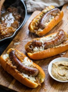 Beer brats on cutting board with bowl of mustard.