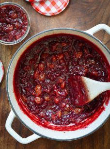 Wooden spoon stirring a Dutch oven of cranberry chutney.