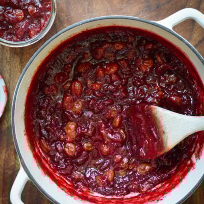 Wooden spoon stirring a Dutch oven of cranberry chutney.
