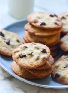 Stacks of thin and crisp chocolate chip cookies on a plate.