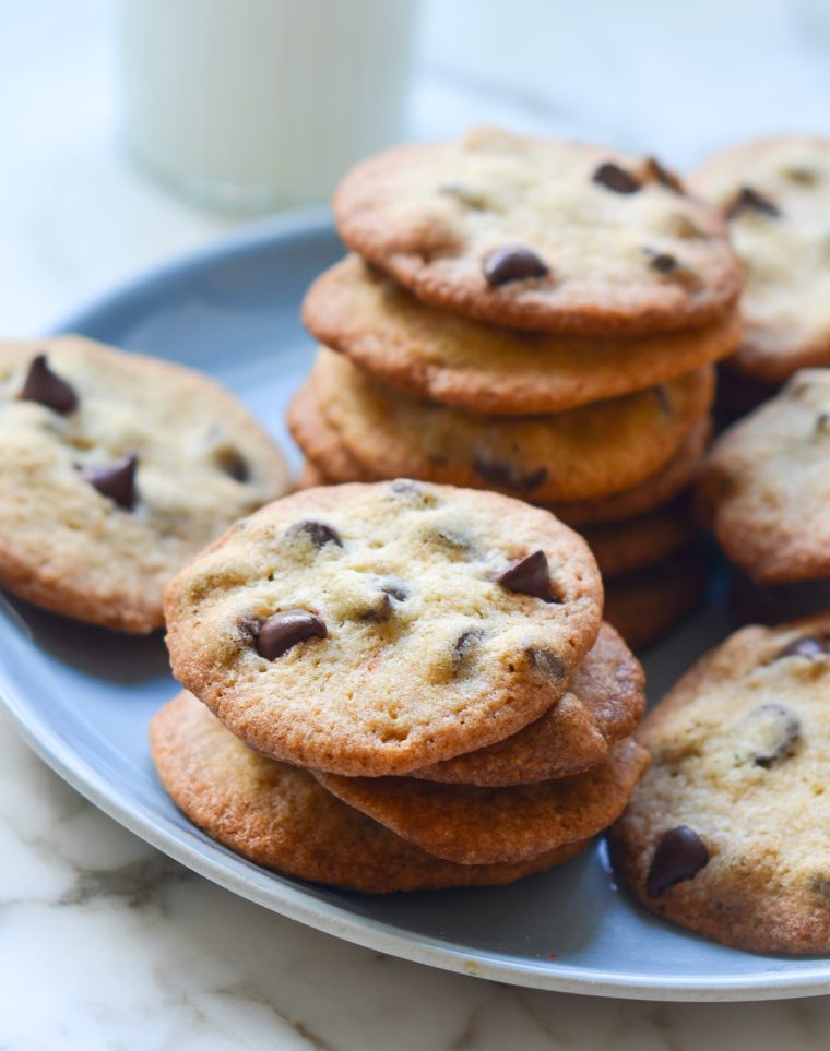 Stacks of thin and crisp chocolate chip cookies on a plate.