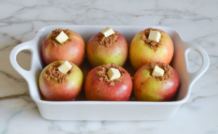 Baking dish of apples stuffed with a brown sugar mixture and topped with butter.