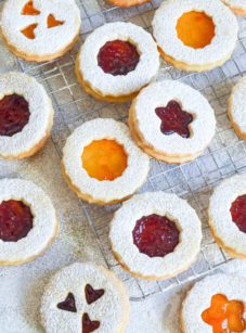 Linzer cookies with various shapes on and around a wire rack.