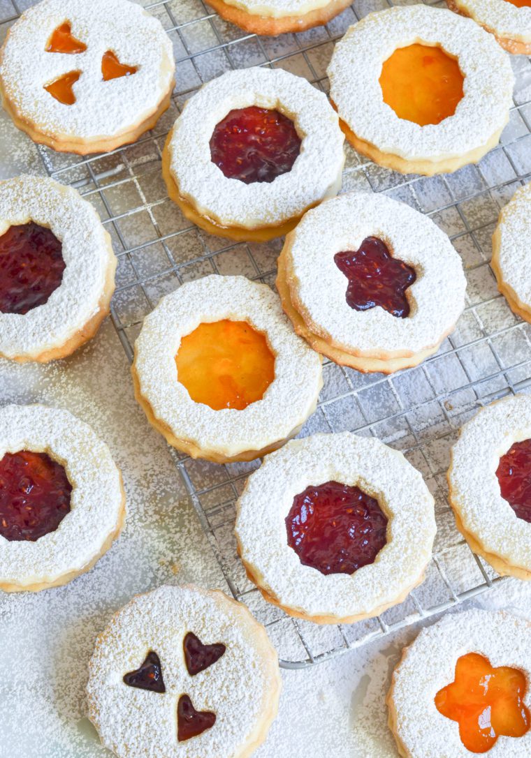 Linzer cookies with various shapes on and around a wire rack.
