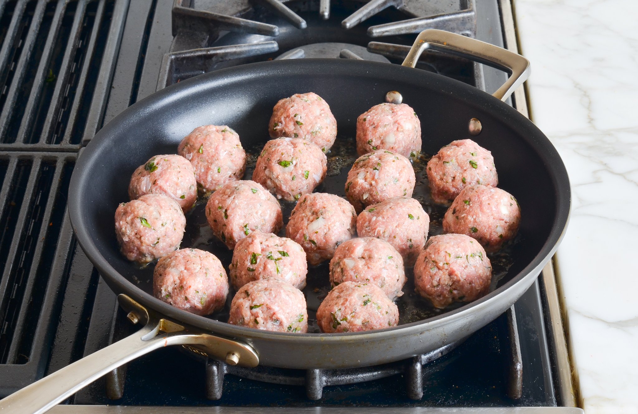 Browning turkey meatballs with oil in a skillet.