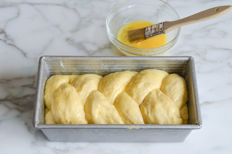 Braided brioche dough in a pan with an egg wash.