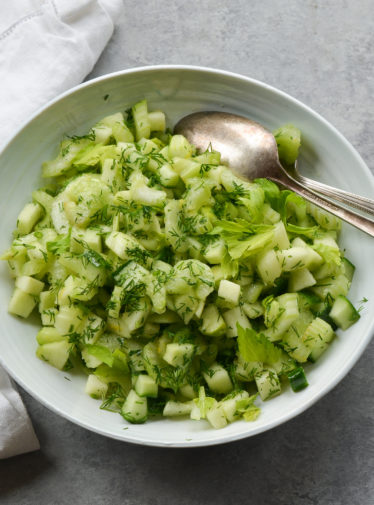 Spoon in a bowl of green apple and celery salad with dill.