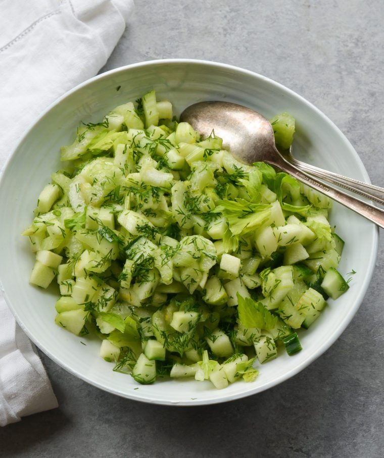 Spoon in a bowl of green apple and celery salad with dill.