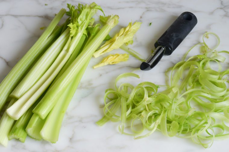 Vegetable peeler with a pile of peeled celery.