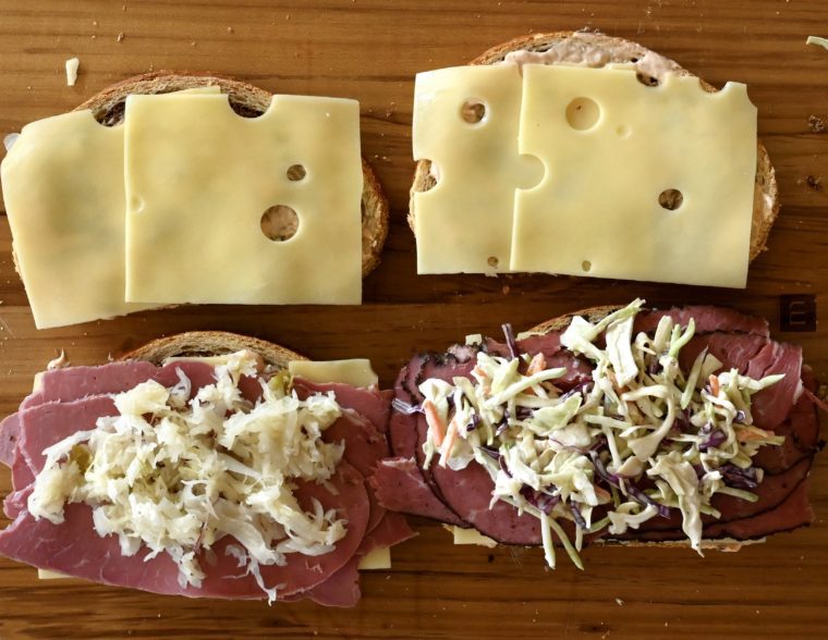 Unassembled reubens on a wooden cutting board.