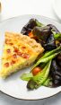 Slice of quiche Lorraine on a plate with a salad.