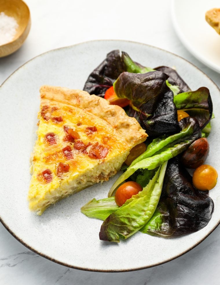 Slice of quiche Lorraine on a plate with a salad.