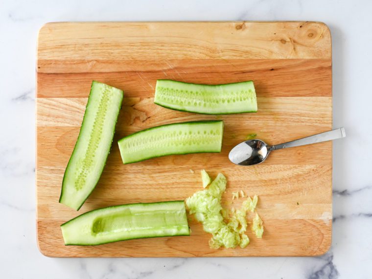 Spoon on a cutting board with cucumbers, once of which has seeds removed.
