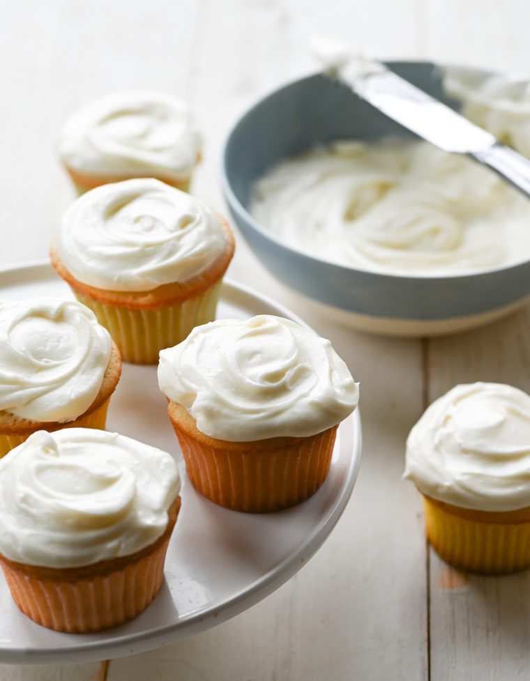 Vanilla cupcakes on and around a raised platter.
