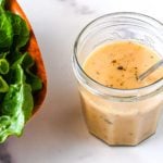 Glass jar of vinaigrette next to a bowl of salad.