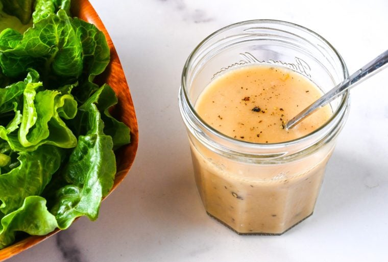 Glass jar of vinaigrette next to a bowl of salad.