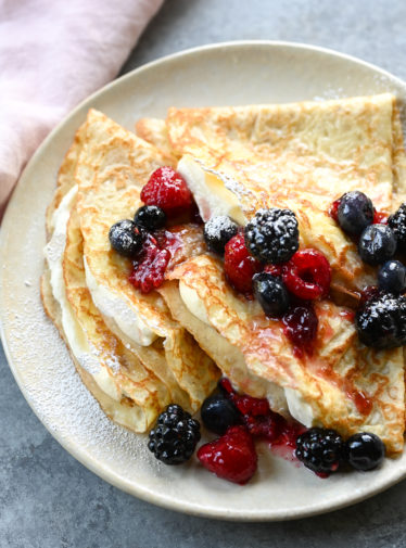 crepes on plate with cream and berries.