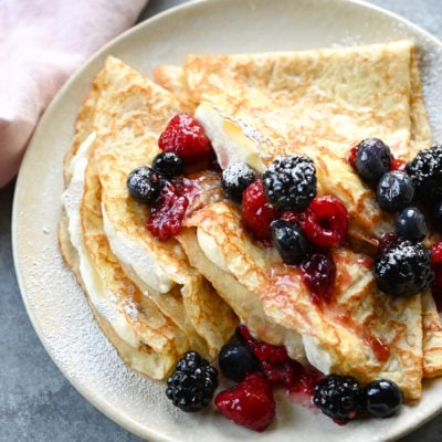 crepes on plate with cream and berries.