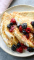 crepes on plate with cream and berries.